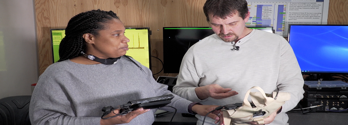 A man and a woman examine a tablet and pieces of a drone.